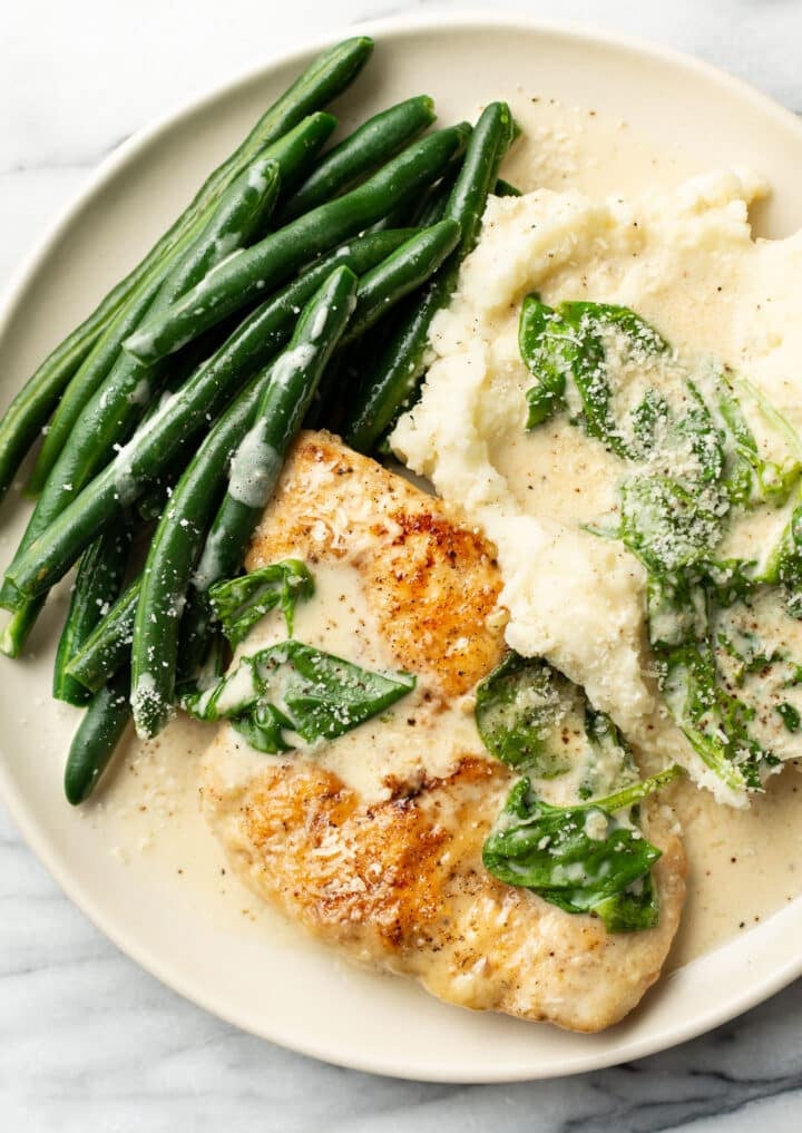 a plate with chicken florentine, green beans, and mashed potatoes with sauce