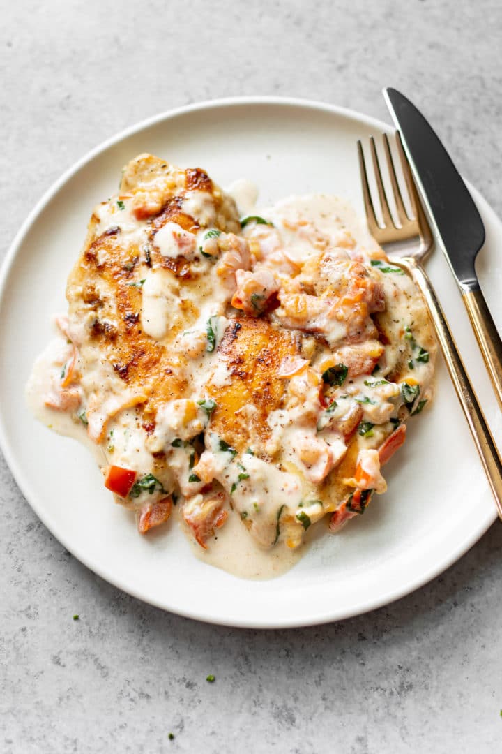 a white plate with tomato basil chicken breasts in a creamy sauce