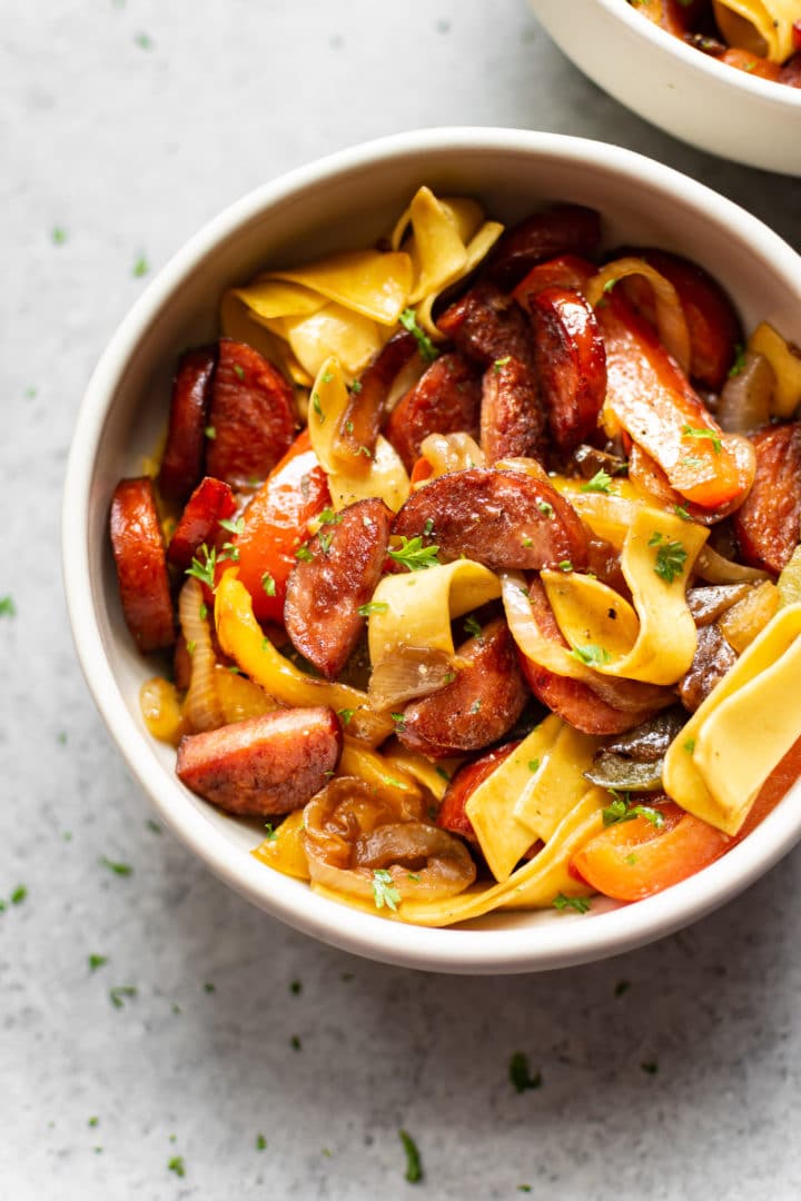 two bowls of sausage and peppers served over egg noodles