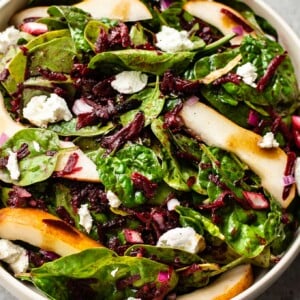 beet and spinach salad with pears, goat cheese, and a balsamic vinaigrette in a beige salad bowl