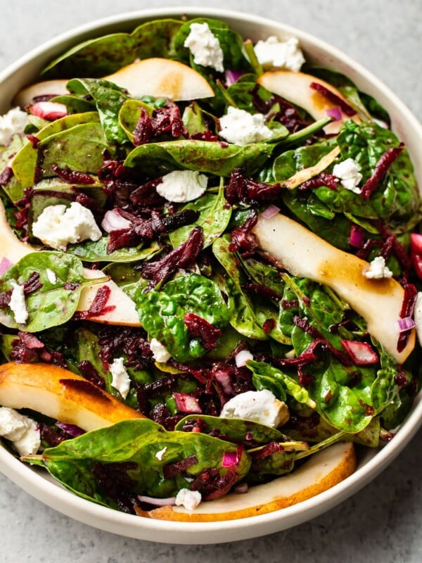 beet and spinach salad with pears, goat cheese, and a balsamic vinaigrette in a beige salad bowl
