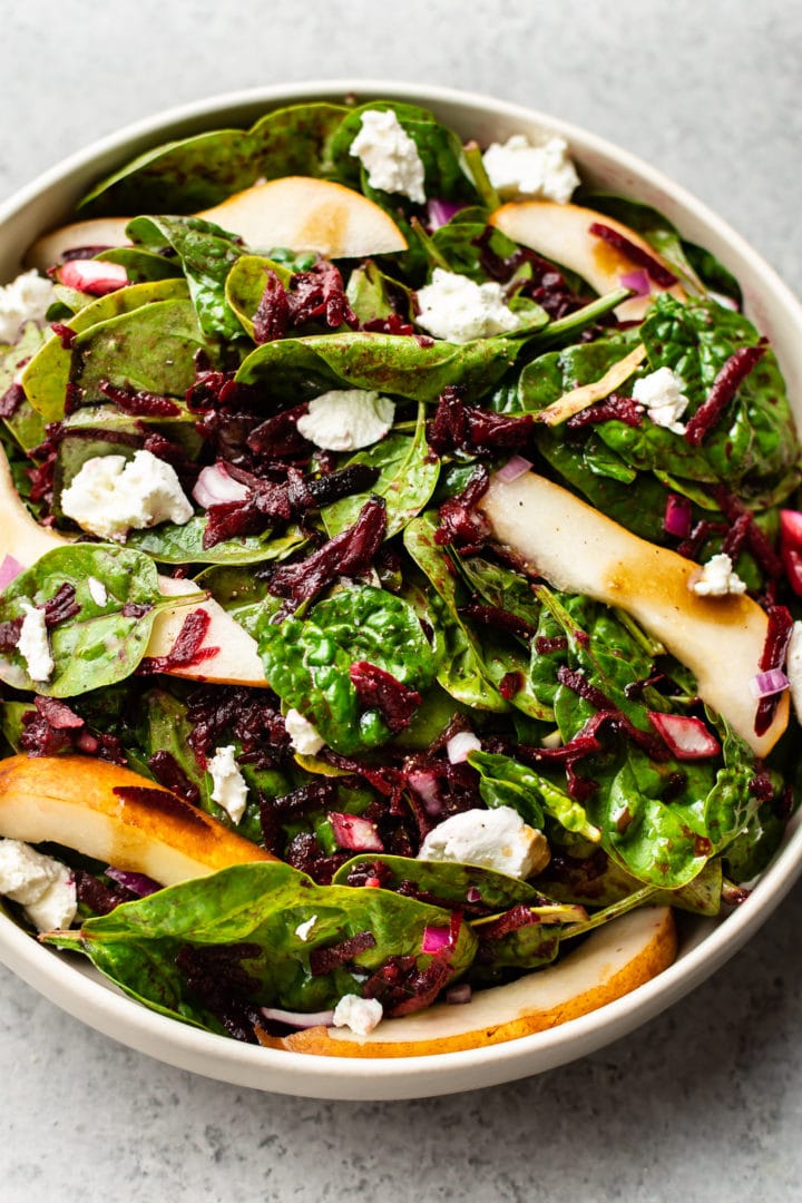 beet and spinach salad with pears, goat cheese, and a balsamic vinaigrette in a beige salad bowl