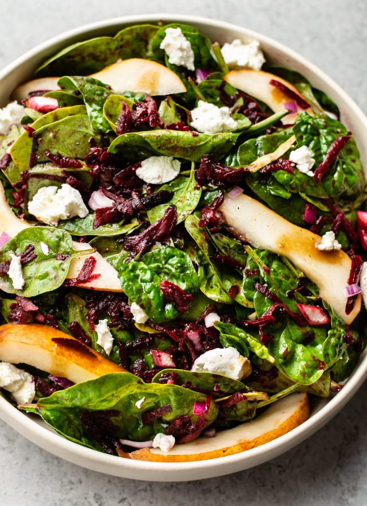 beet and spinach salad with pears, goat cheese, and a balsamic vinaigrette in a beige salad bowl