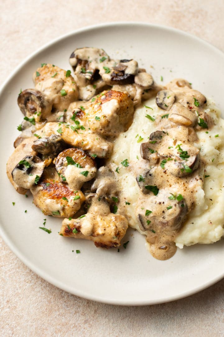 chicken stroganoff on a beige plate with mashed potatoes and lots of sauce