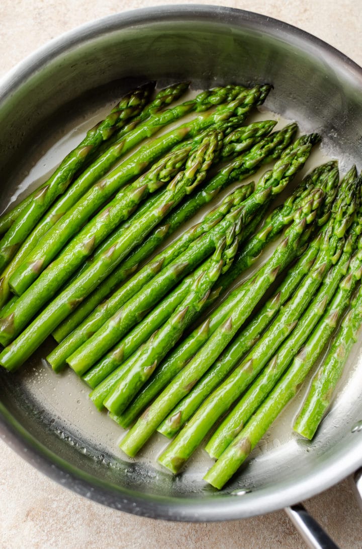 poached asparagus in a pan with buttery poaching liquid