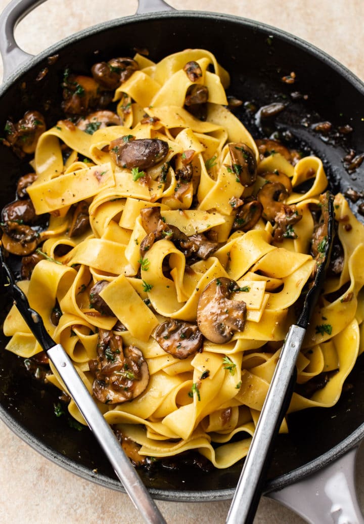 garlic butter mushroom pasta in a skillet with tongs to serve