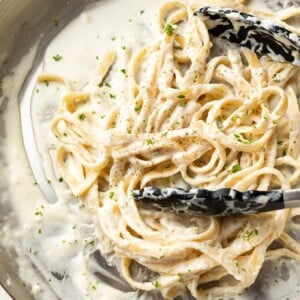 a skillet with fettuccine alfredo and serving tongs
