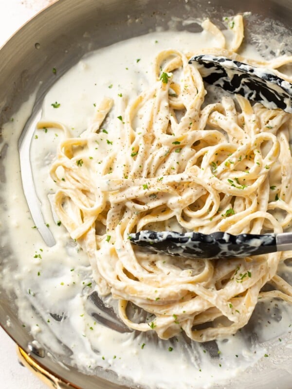 a skillet with fettuccine alfredo and serving tongs