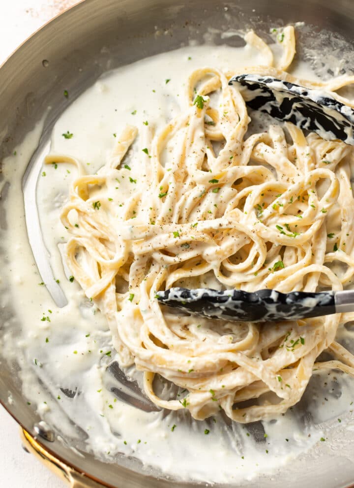 a skillet with fettuccine alfredo and serving tongs