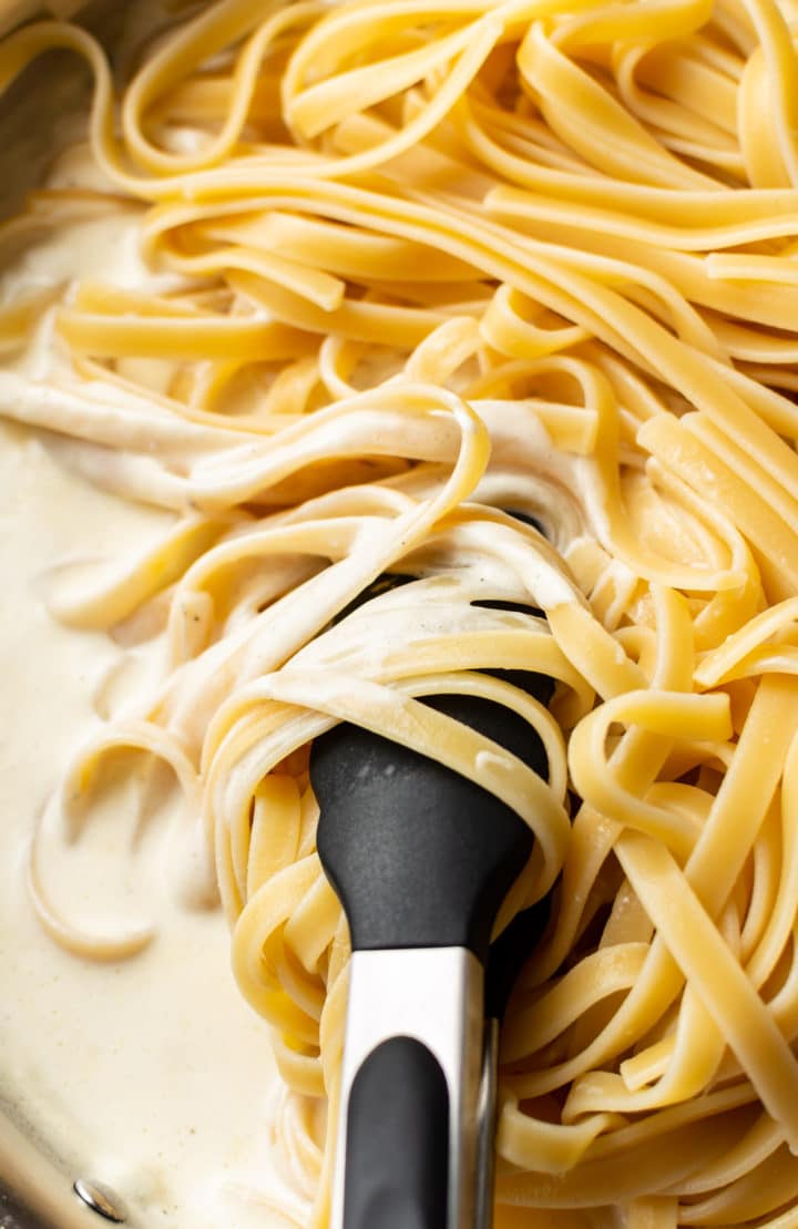 close-up of fettuccine noodles being tossed with Alfredo sauce (with tongs)