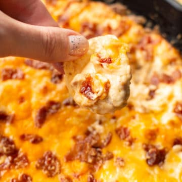 holding a chip scooping cheddar bacon dip from skillet