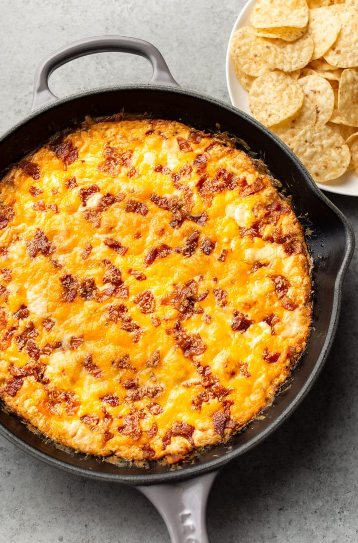 cheddar bacon dip in a cast iron skillet with chips on the side