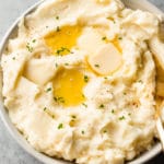 the best garlic mashed potatoes in a beige bowl with plenty of butter on top!