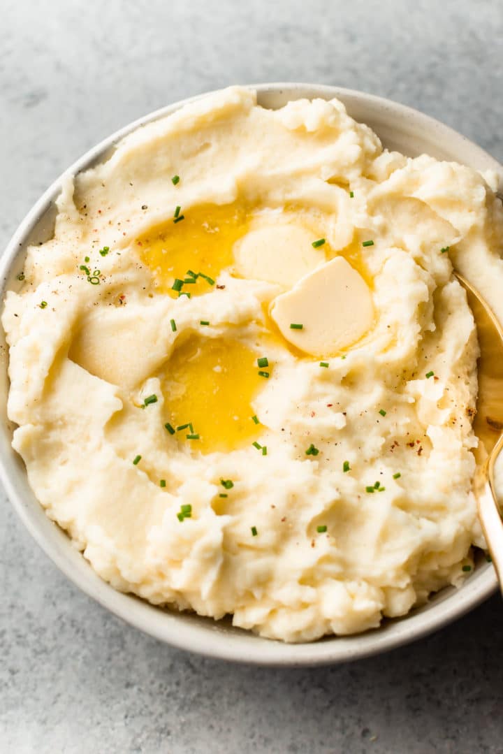 the best garlic mashed potatoes in a beige bowl with plenty of butter on top!