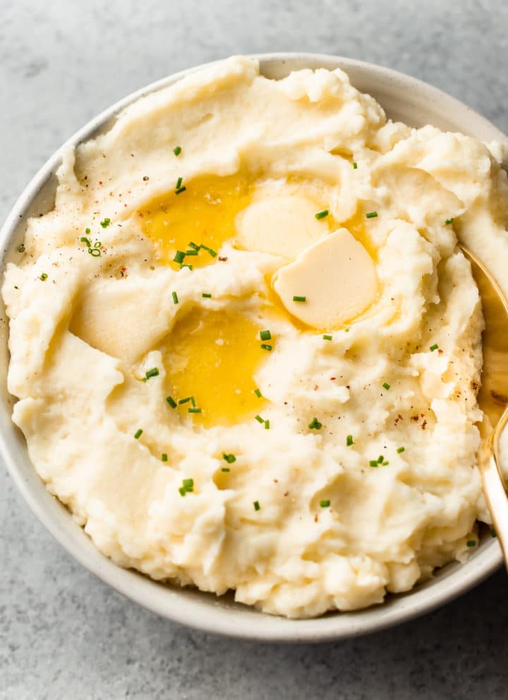the best garlic mashed potatoes in a beige bowl with plenty of butter on top!