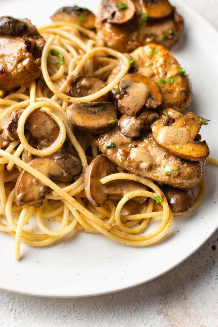 pork marsala on a white plate served over spaghetti