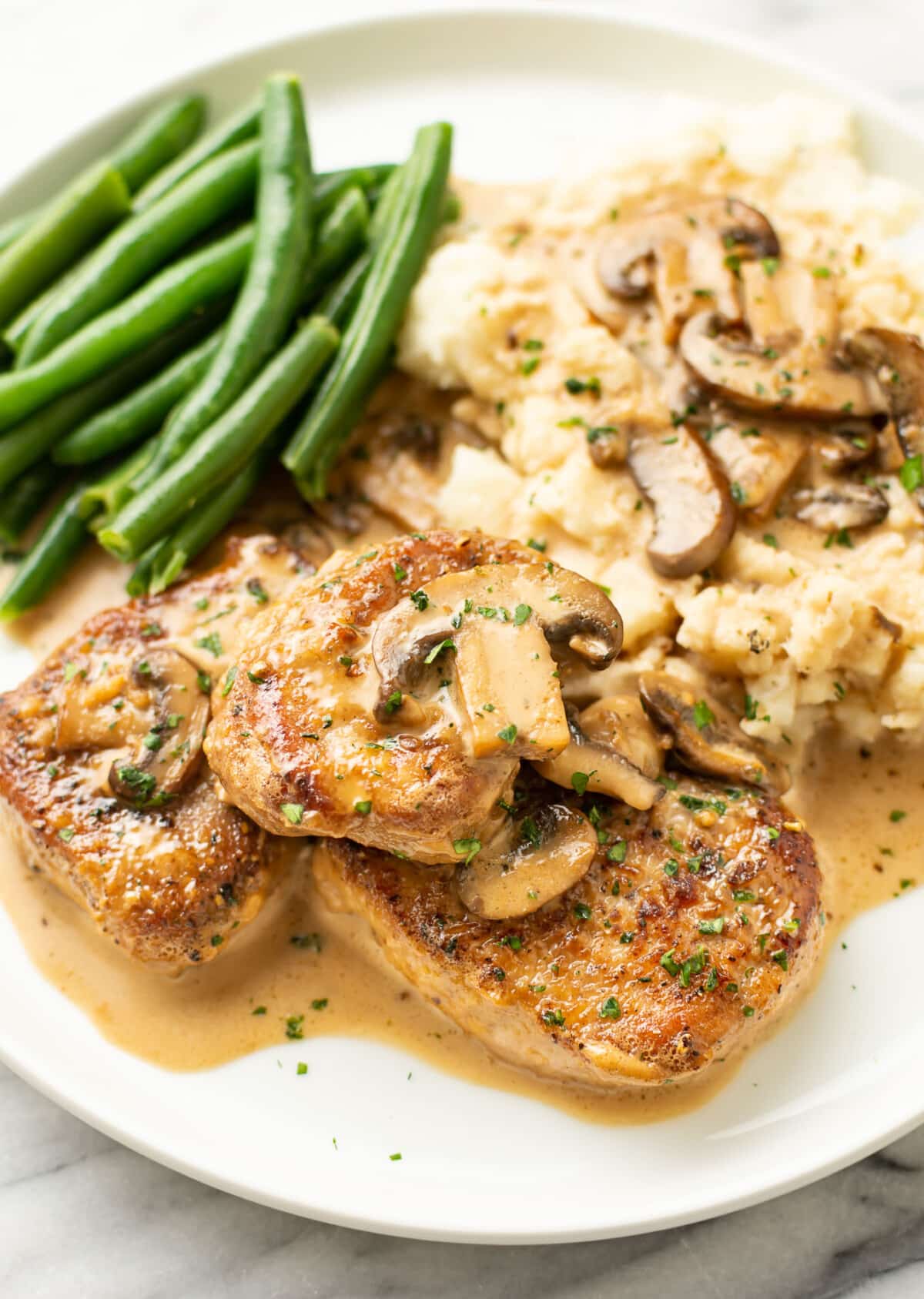 a plate with pork tenderloin marsala, mashed potatoes, and green beans
