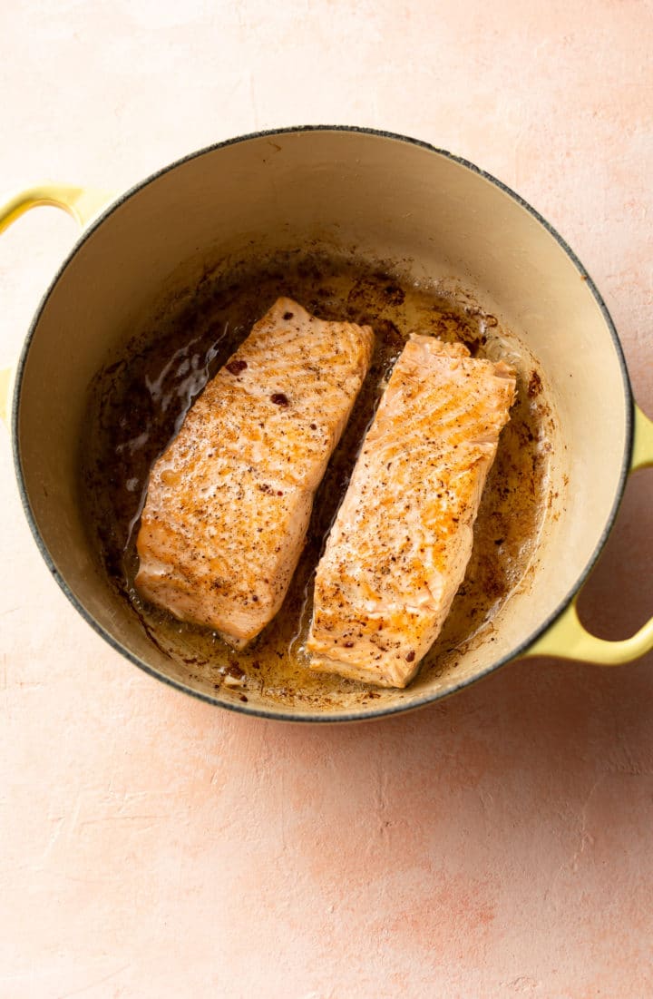two pieces of salmon seared in a yellow Le Creuset pot