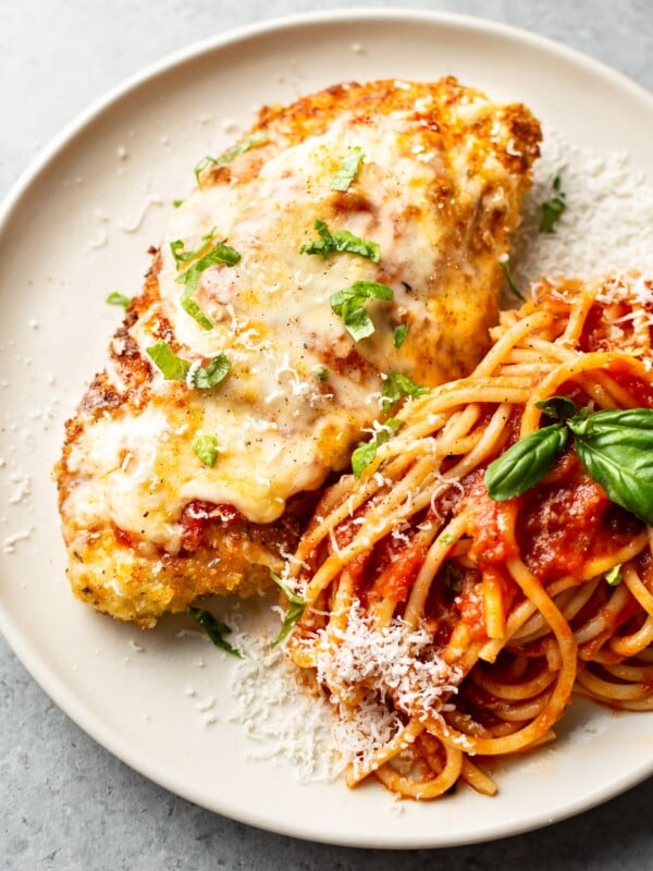 chicken parmesan on a plate with spaghetti tossed with marinara sauce and fresh basil and parmesan grated on top