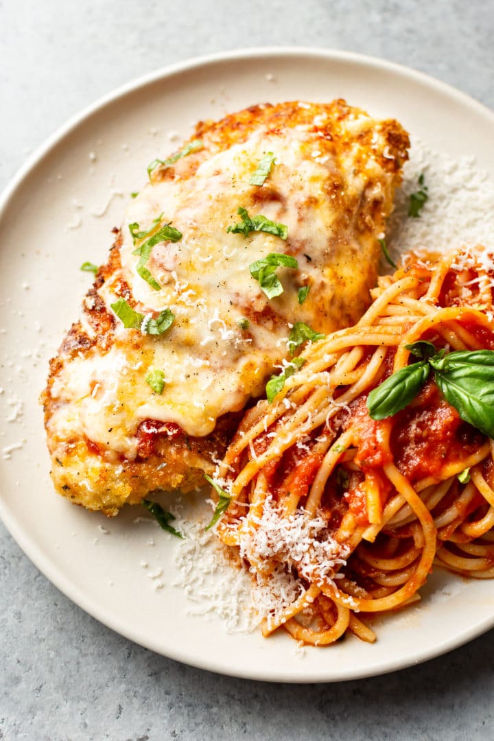 chicken parmesan on a plate with spaghetti tossed with marinara sauce and fresh basil and parmesan grated on top