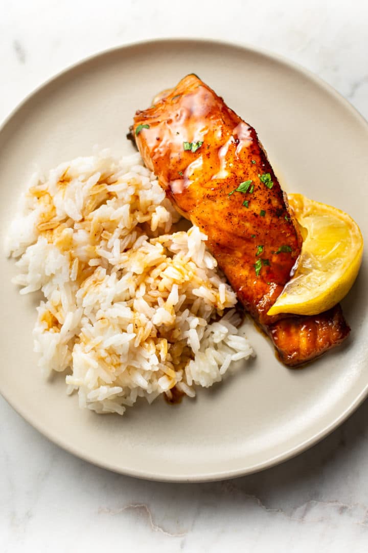 honey glazed salmon on a plate with rice and a lemon wedge