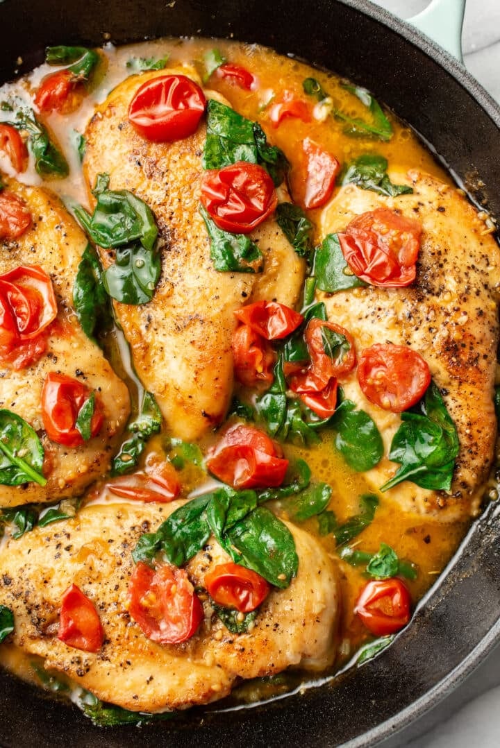 a cast iron skillet with tomato spinach white wine chicken