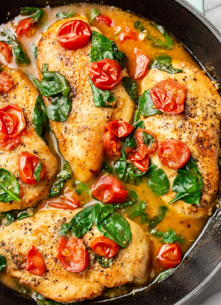 a cast iron skillet with tomato spinach white wine chicken