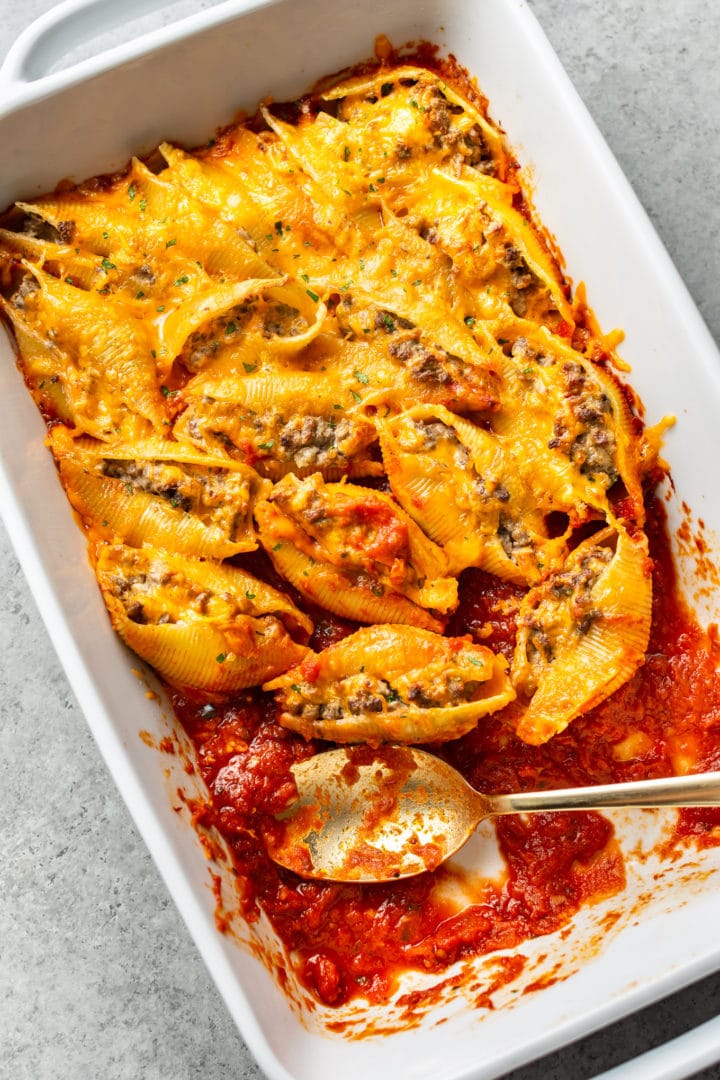 ground beef stuffed shells in a white baking dish with a few stuffed shells missing