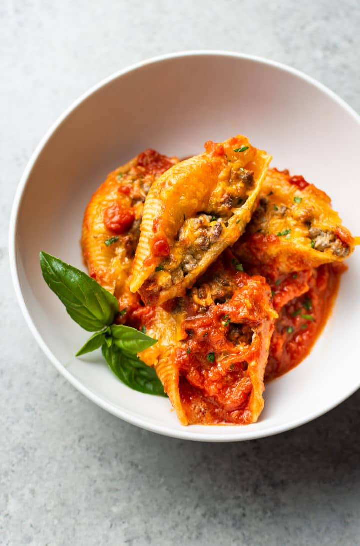 beef stuffed shells in a white bowl with a sprig of fresh basil