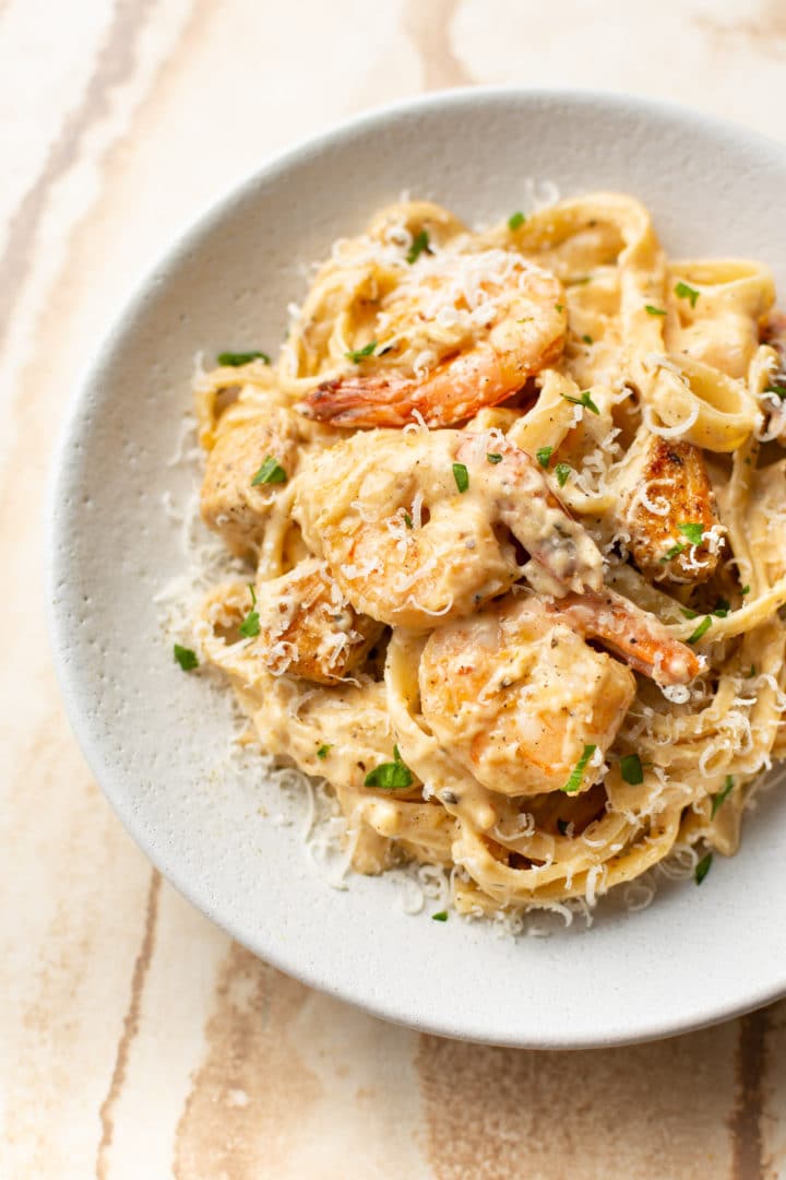 Cajun chicken and shrimp pasta (with fettuccine) smothered in Alfredo sauce in a white bowl