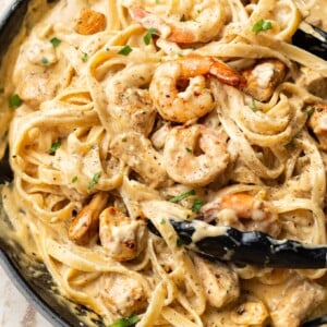 Cajun chicken and shrimp Alfredo in a skillet (being tossed with cooking tongs)