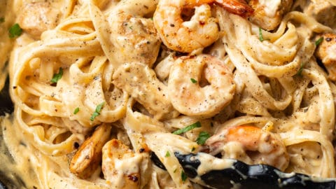 Cajun chicken and shrimp Alfredo in a skillet (being tossed with cooking tongs)