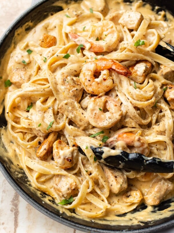 Cajun chicken and shrimp Alfredo in a skillet (being tossed with cooking tongs)