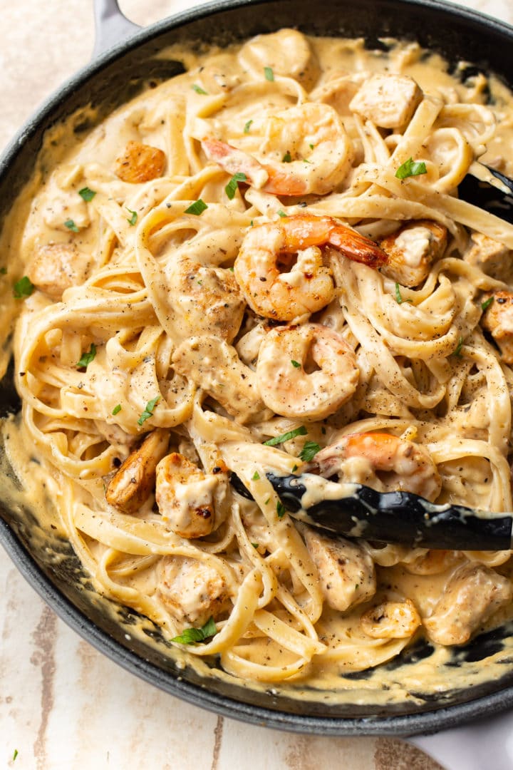 Cajun chicken and shrimp Alfredo in a skillet (being tossed with cooking tongs)