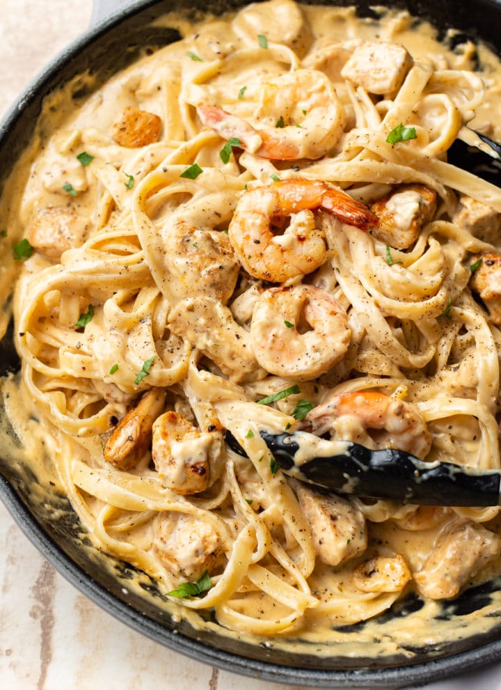 Cajun chicken and shrimp Alfredo in a skillet (being tossed with cooking tongs)