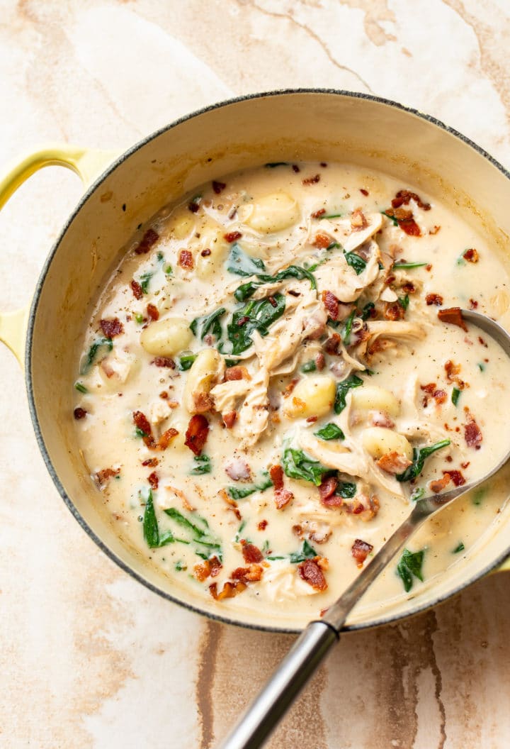 creamy chicken gnocchi soup with bacon and spinach in a yellow pot