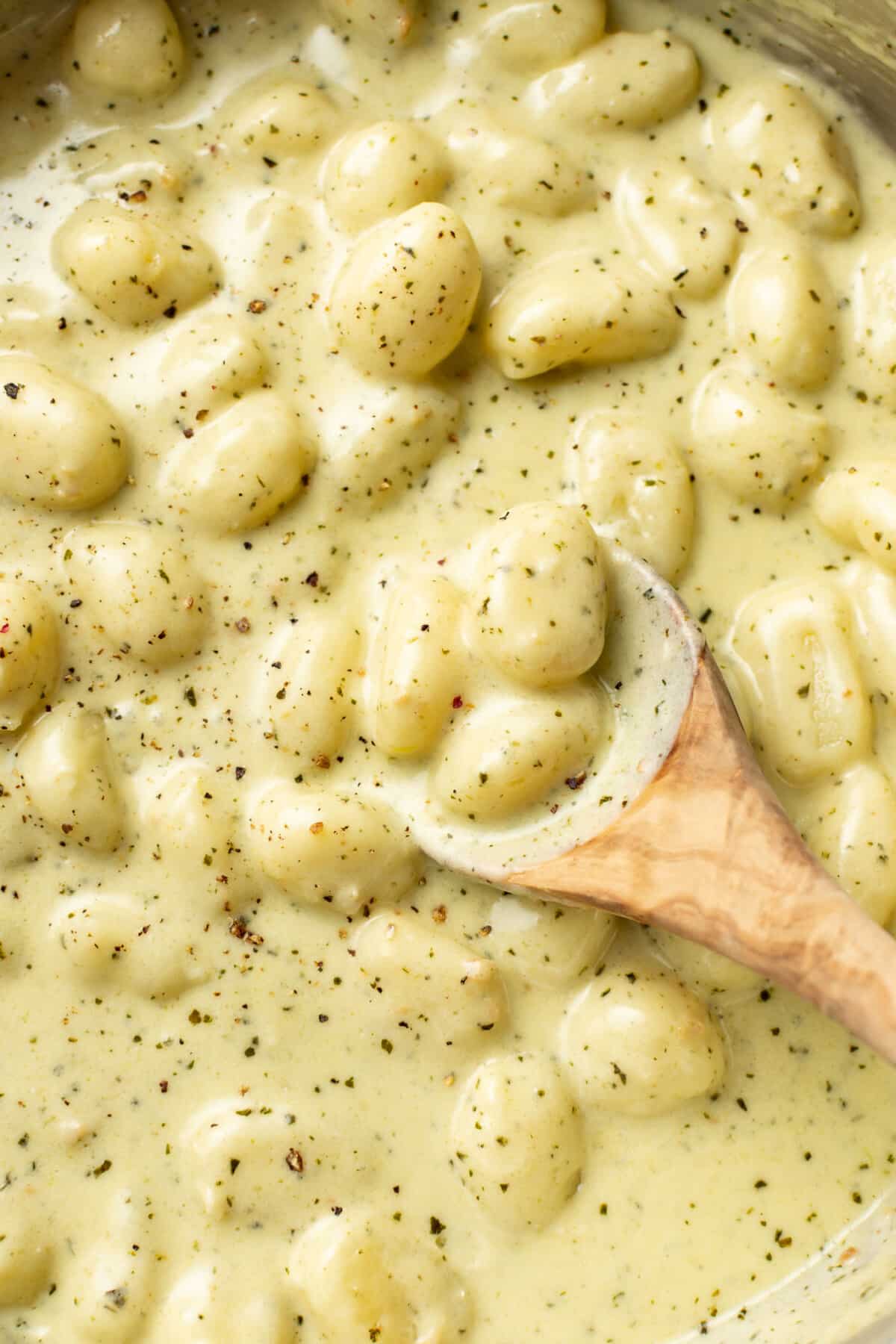 closeup of a pan with creamy pesto gnocchi and a wooden spoon