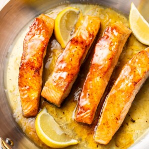 honey lemon butter salmon in a skillet with fresh lemon wedges