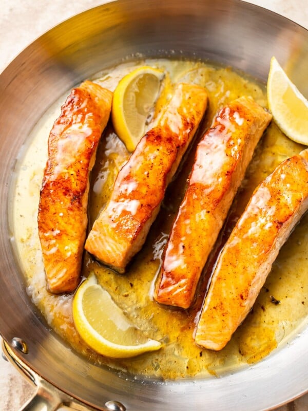 honey lemon butter salmon in a skillet with fresh lemon wedges