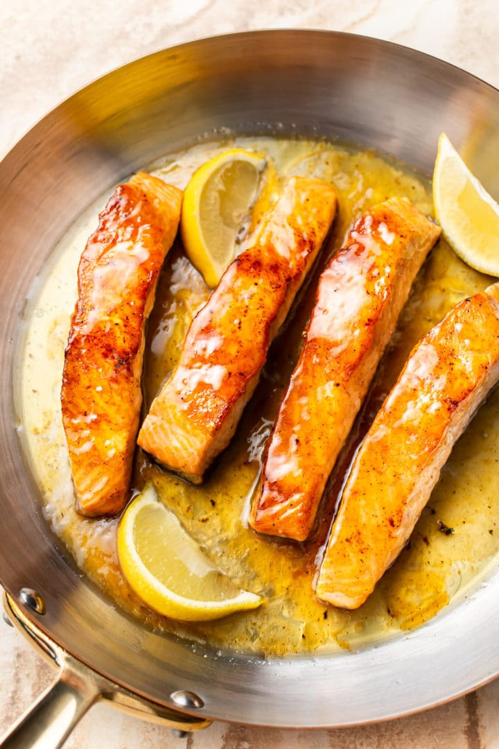 honey lemon butter salmon in a skillet with fresh lemon wedges