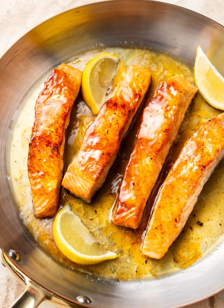 honey lemon butter salmon in a skillet with fresh lemon wedges
