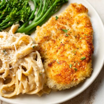 crispy parmesan crusted chicken on a plate with Fettuccine Alfredo and broccolini