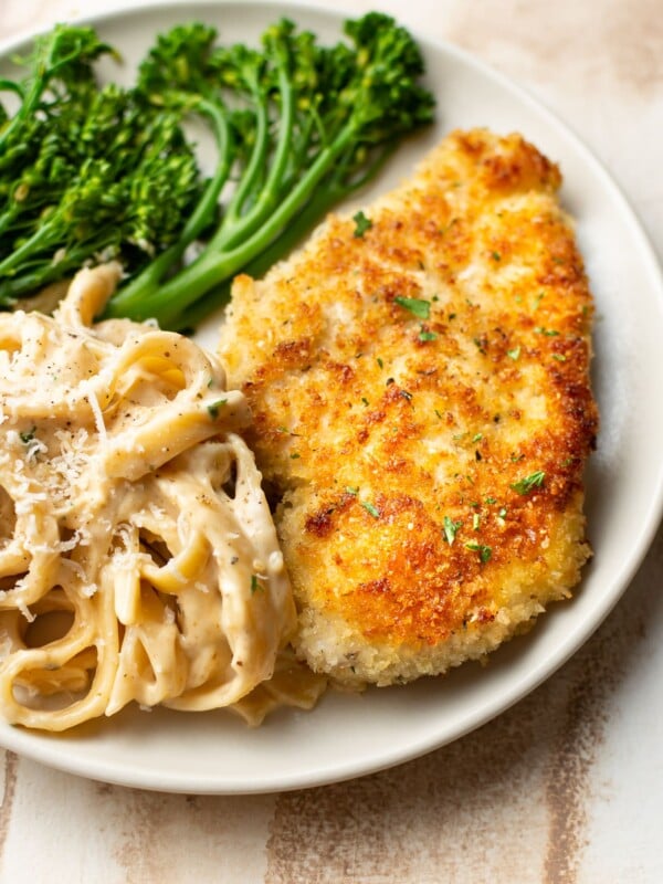 crispy parmesan crusted chicken on a plate with Fettuccine Alfredo and broccolini