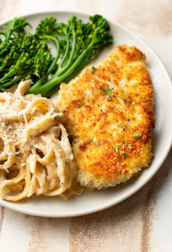 crispy parmesan crusted chicken on a plate with Fettuccine Alfredo and broccolini