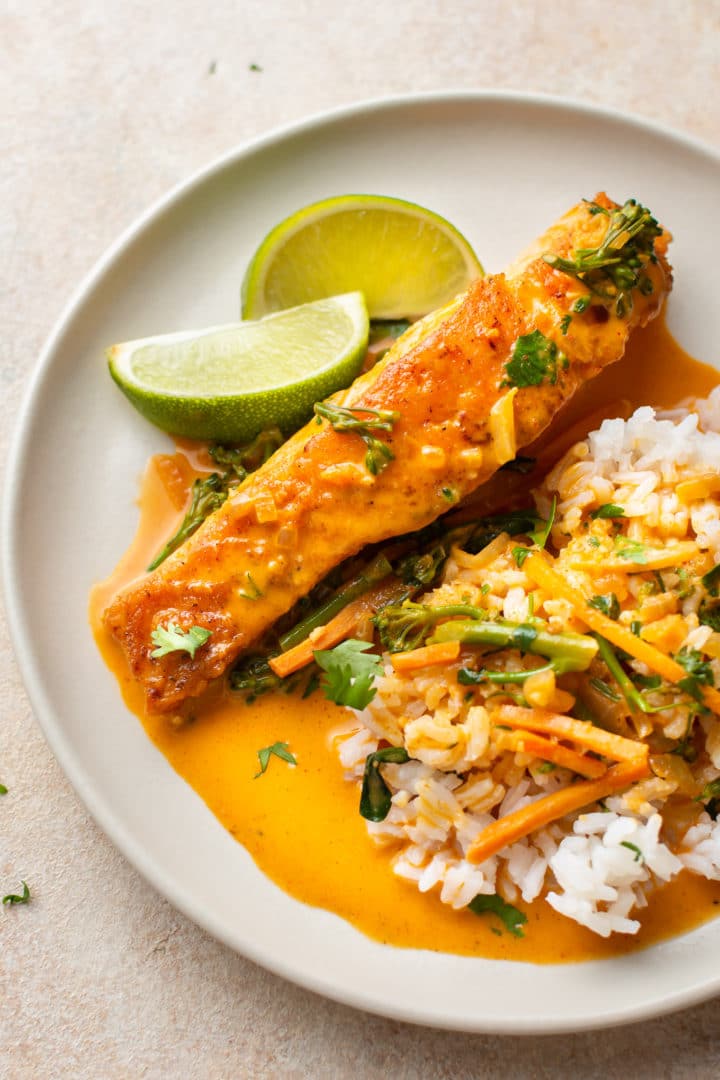 Thai coconut curry salmon on a plate with rice, tons of sauce, and lime wedges
