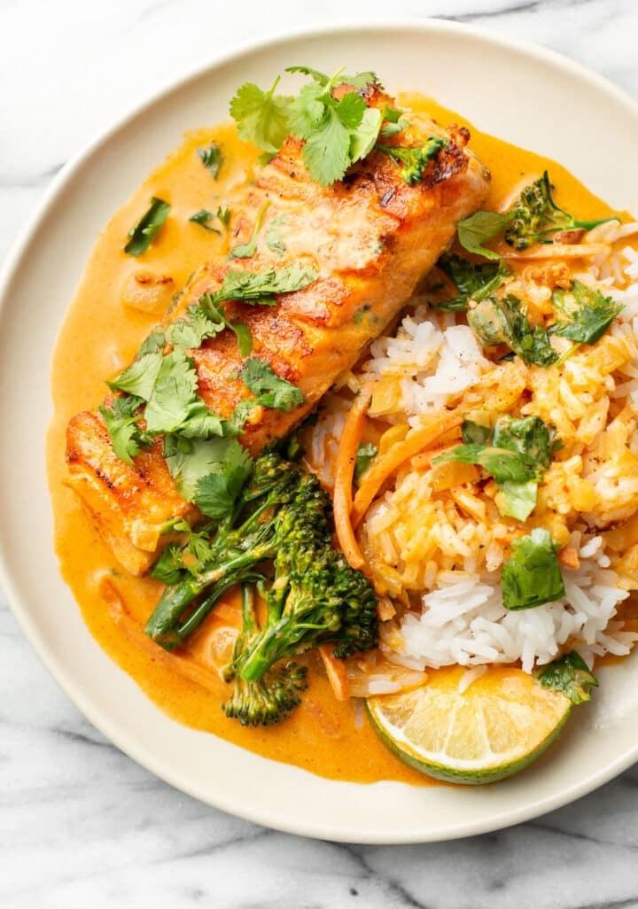 a plate with salmon red curry over jasmine rice with a lime wedge