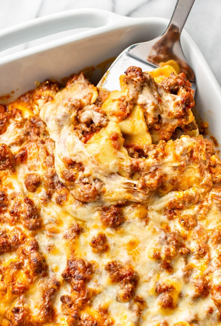 close-up of cheesy baked ravioli casserole (in baking dish with some being lifted out with spatula)