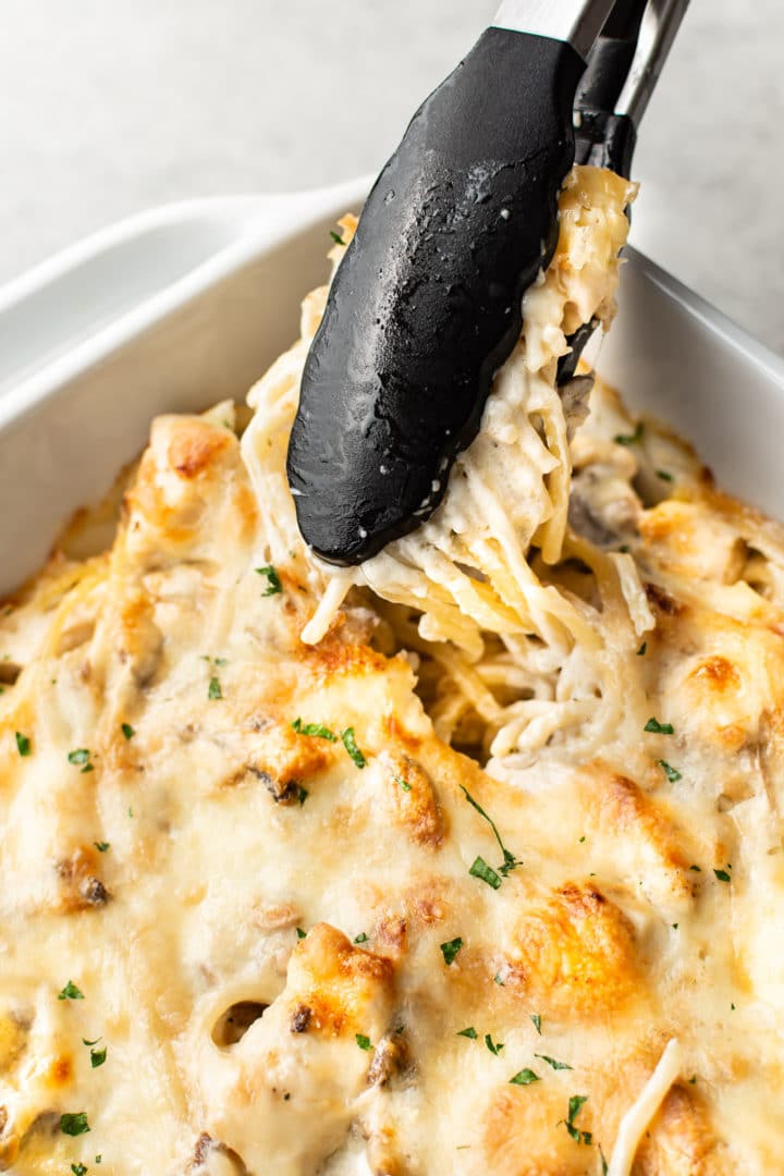 creamy Chicken Tetrazzini in a baking dish with cooking tongs grabbing some