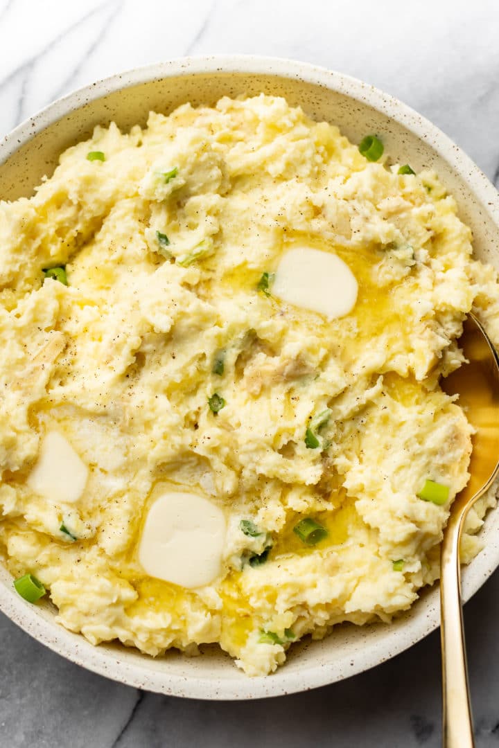 close-up of cream cheese mashed potatoes in a serving bowl with a gold spoon