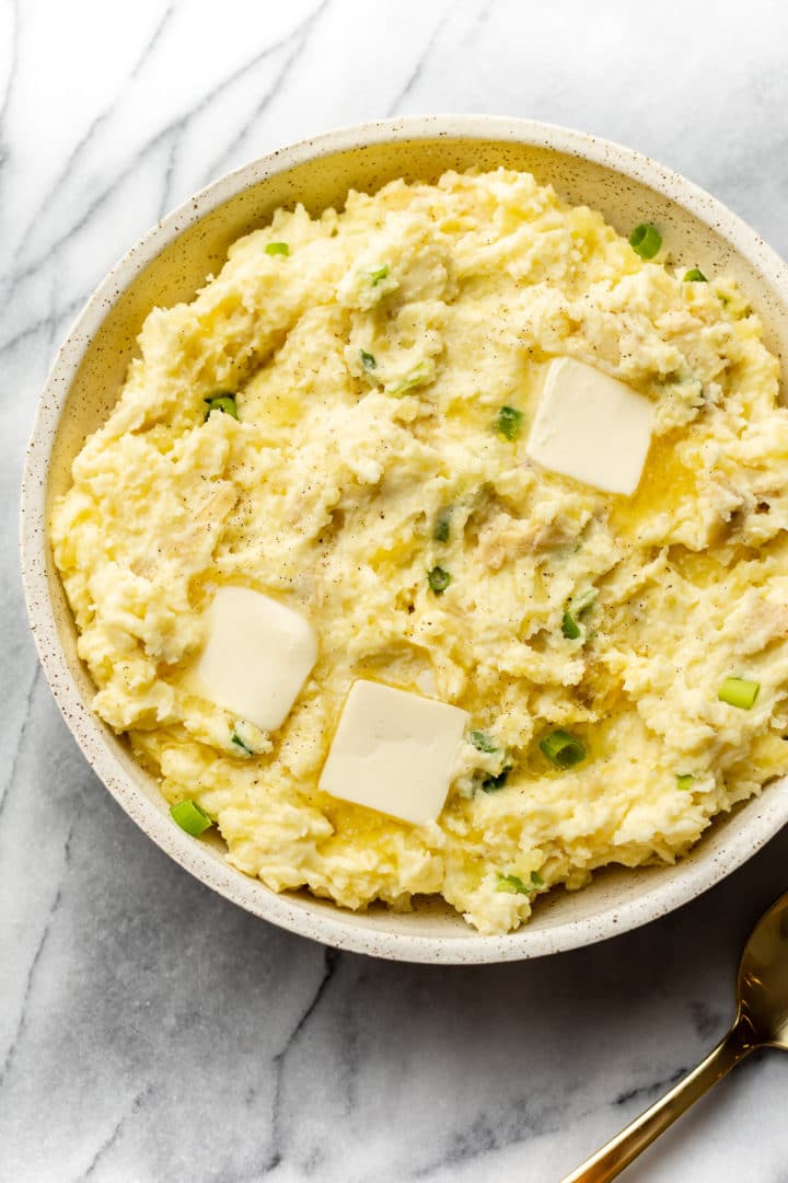 the best cream cheese mashed potatoes in a serving bowl with pats of butter on top